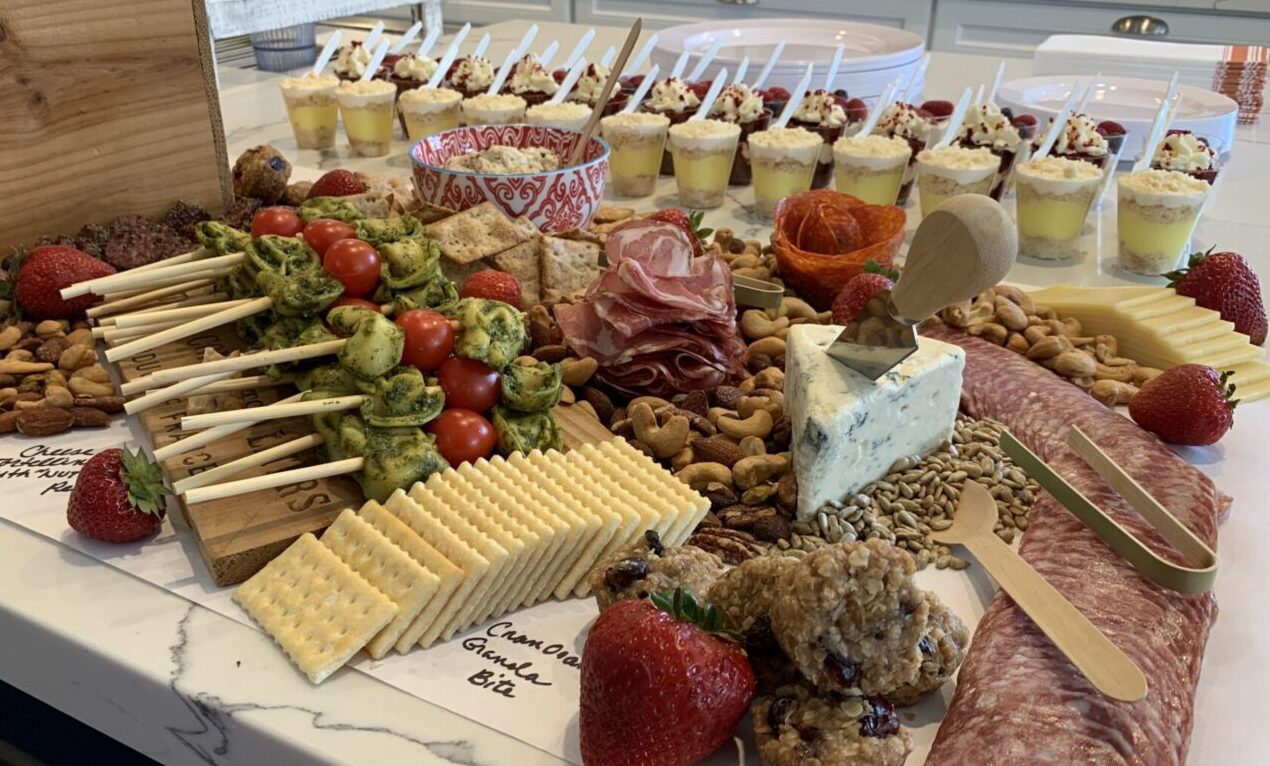 A charcuterie board with meats, cheeses, crackers, and fruit on a kitchen counter.