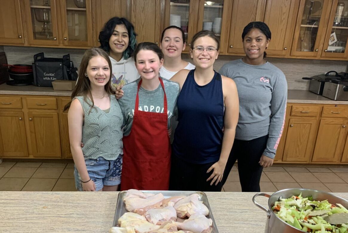 A group of six women smiling together in a kitchen.