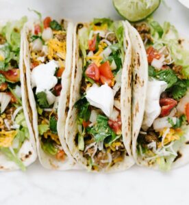 Three soft tacos filled with chicken, lettuce, cheese, tomatoes, and sour cream.