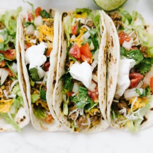 Three soft tacos filled with chicken, lettuce, cheese, tomatoes, and sour cream.