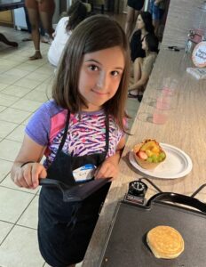 Young girl cooking a pancake on a griddle with a smile.