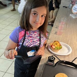 Young girl cooking a pancake on a griddle with a smile.