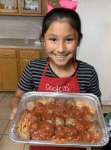 A girl proudly holds a tray of homemade meatballs in sauce.