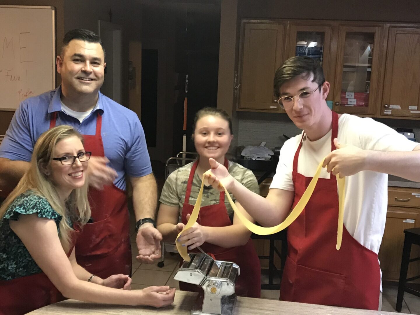 Four people cooking together, holding long pasta noodles.