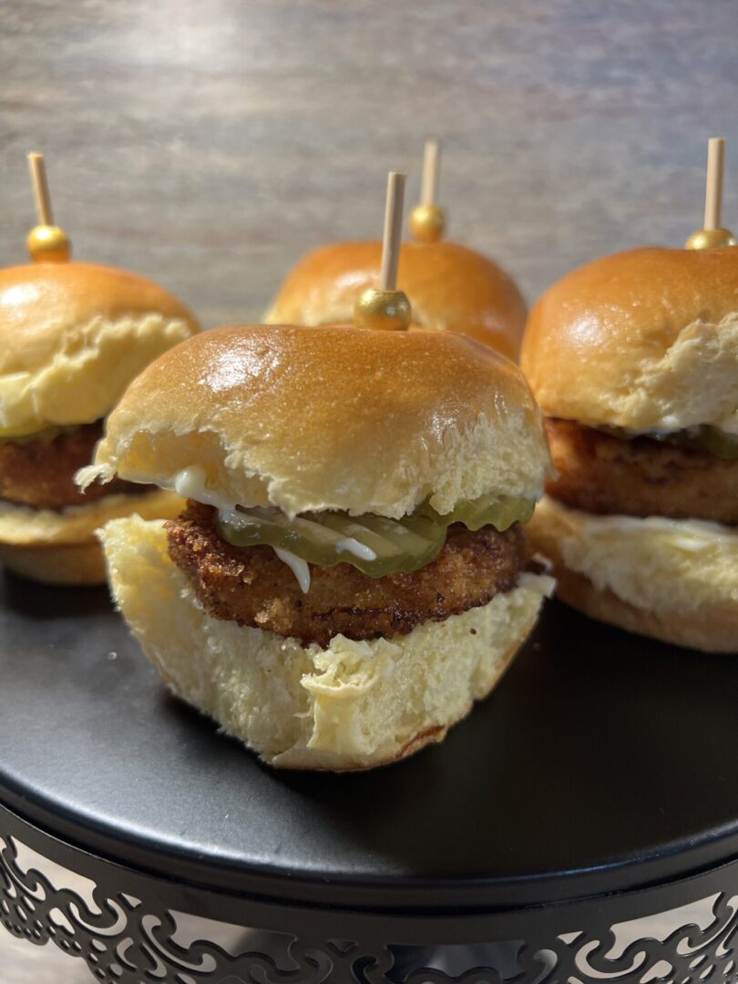 Close-up of mini burgers with lettuce and sauce on a black plate.