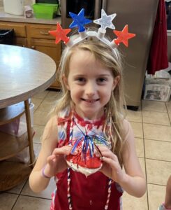 Young girl wearing star headband holds a patriotic craft.