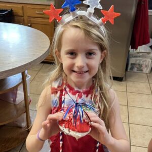 Young girl wearing star headband holds a patriotic craft.