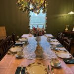 Elegantly set dining table with floral centerpiece and vintage china in a warmly lit room.